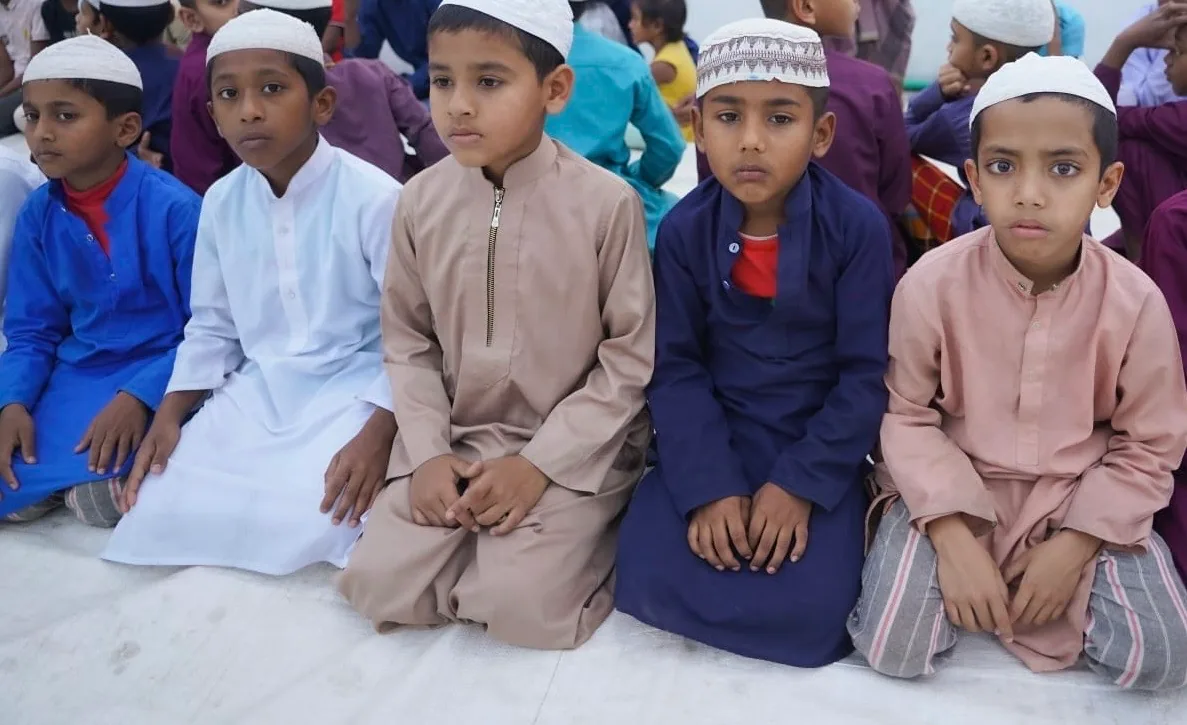Five orphan boys in prayer attire sitting in row at the campus